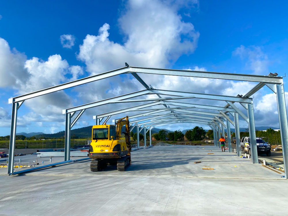 Steel portal frames being erected for an industrial shed, with purlins staged for installation